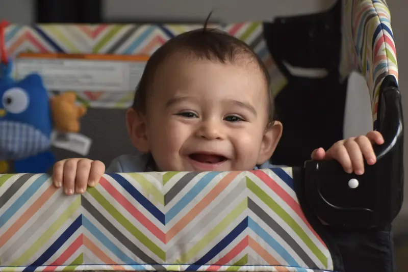 A joyful baby smiling from a playpen adorned with colorful chevron patterns