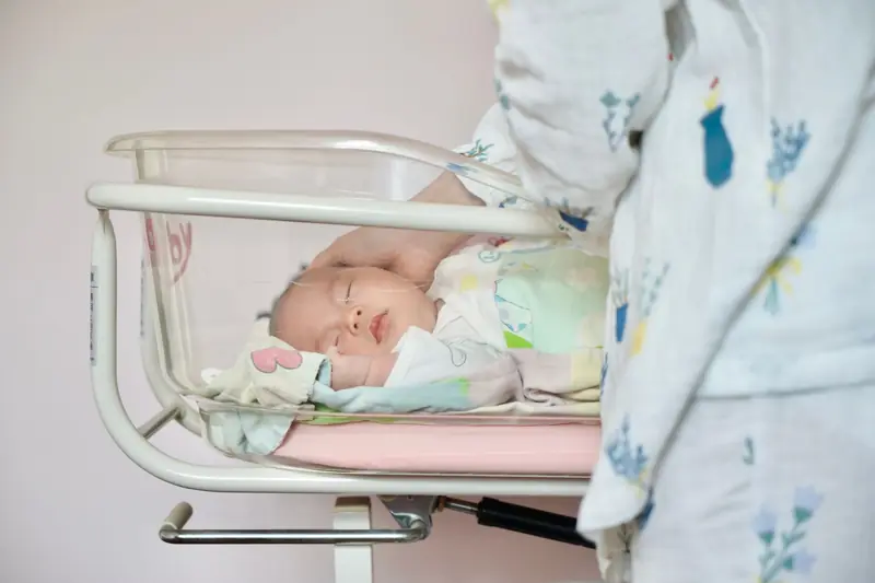 A tender moment of a newborn baby sleeping peacefully in a hospital bassinet being gently touched by a parent