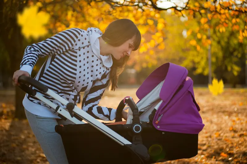 A mother smiling down at her baby in a stroller during an autumn stroll in a park