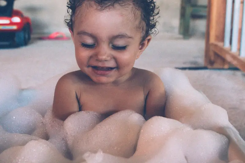 Candid shot of a smiling baby enjoying a bubble bath indoors, captured in a warm and playful atmosphere