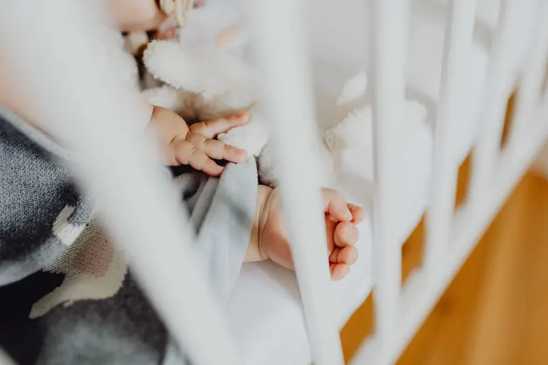 Adorable baby sleeping peacefully in a crib, holding a soft toy next to a baby blanket