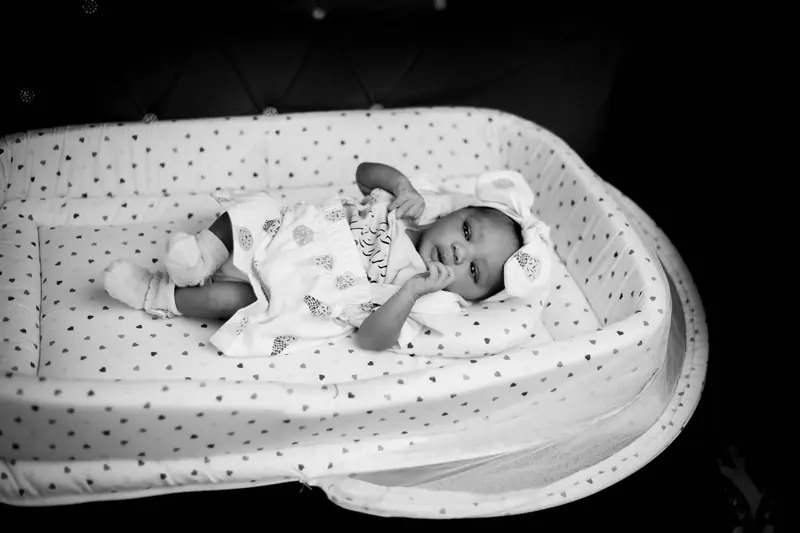 Charming black and white photo of a baby resting in a patterned bassinet