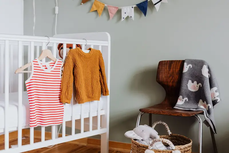 Warm and inviting nursery featuring a crib with knit sweater and striped dress on hangers