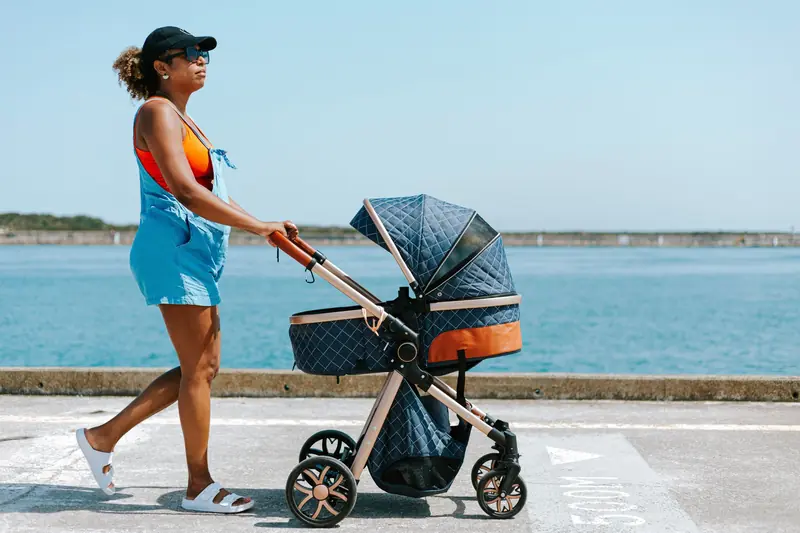 Woman in casual attire strolling with a baby stroller along a seaside path
