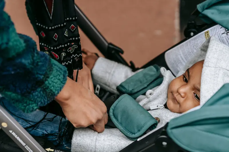 Crop anonymous ethnic mother adjusting clothes of baby lying in stroller and looking away on street in daytime