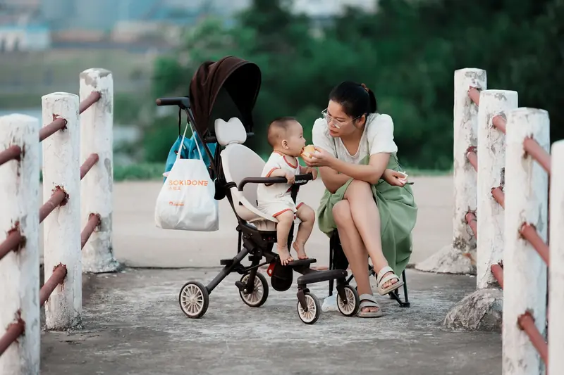 A mother lovingly feeds her baby while sitting outdoors with a stroller