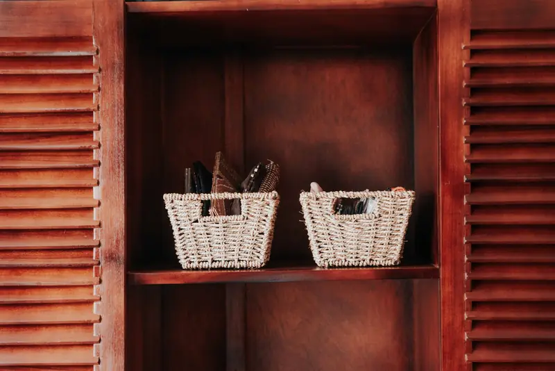 Two woven baskets on a wooden shelf within a cabinet, providing storage decor