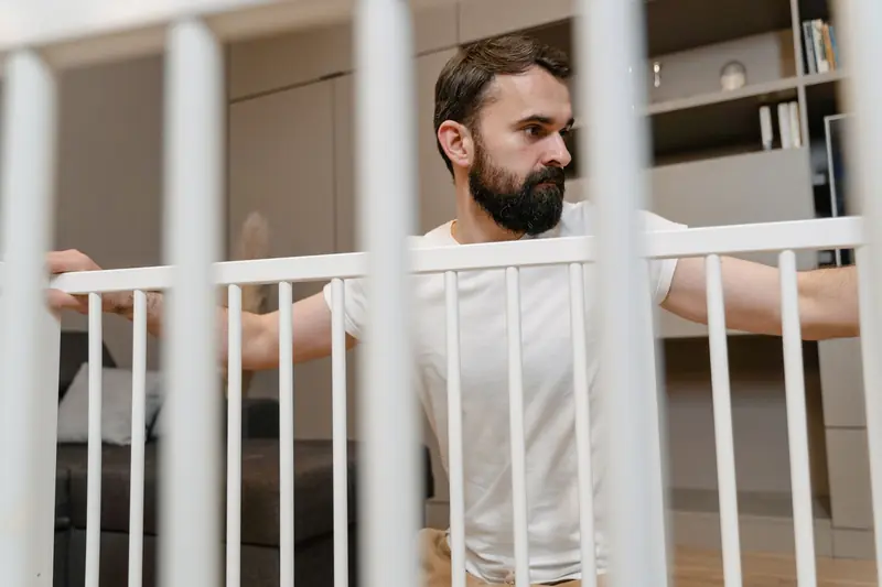 Bearded man in white t-shirt assembling a white baby crib indoors