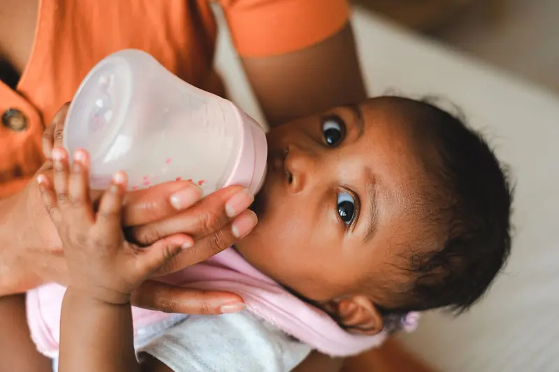 Close-up of a mother feeding her baby with a milk bottle indoors