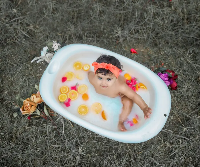 Cute baby enjoying an outdoor milk bath with flowers and citrus slices in a tub