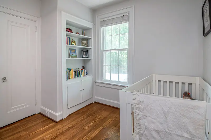 Simple and inviting nursery room with a crib, wooden flooring, and built-in bookshelves