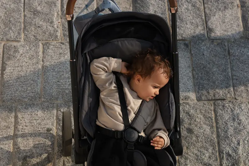 Overhead view of a baby in a stroller on a stone pavement, enjoying a sunny day